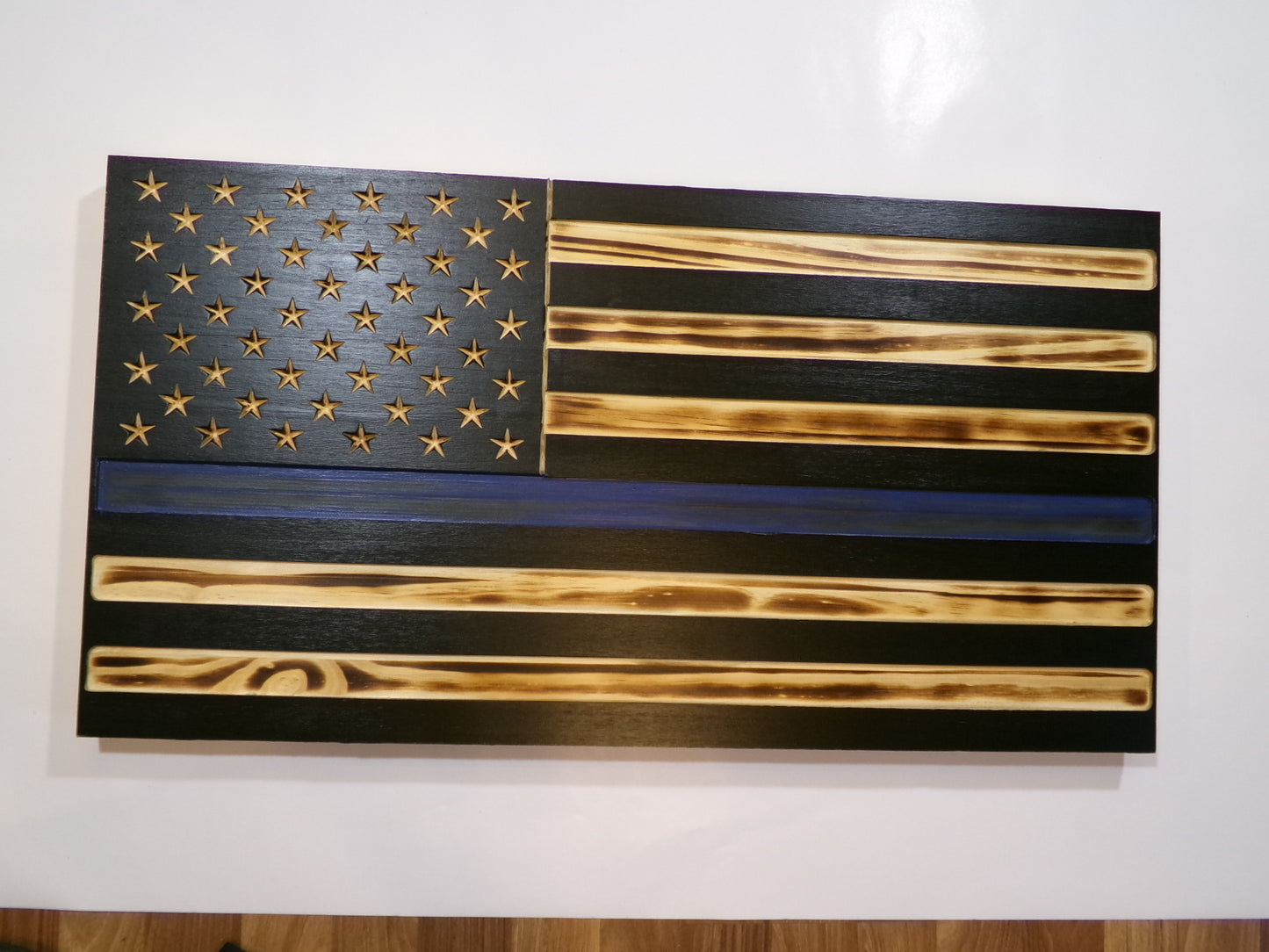 These wooden American blue line flags are locally sourced from pine and finished with environmentally responsible products. The rustic torched finish shows a unique flair making each piece completely special. Stars are carved not merely painted or applied. The proprietary hanger design incorporates a heavy-duty cable system for mounting. The full sized 30" x 16" flags are large enough to be a focal point in any room or man cave.